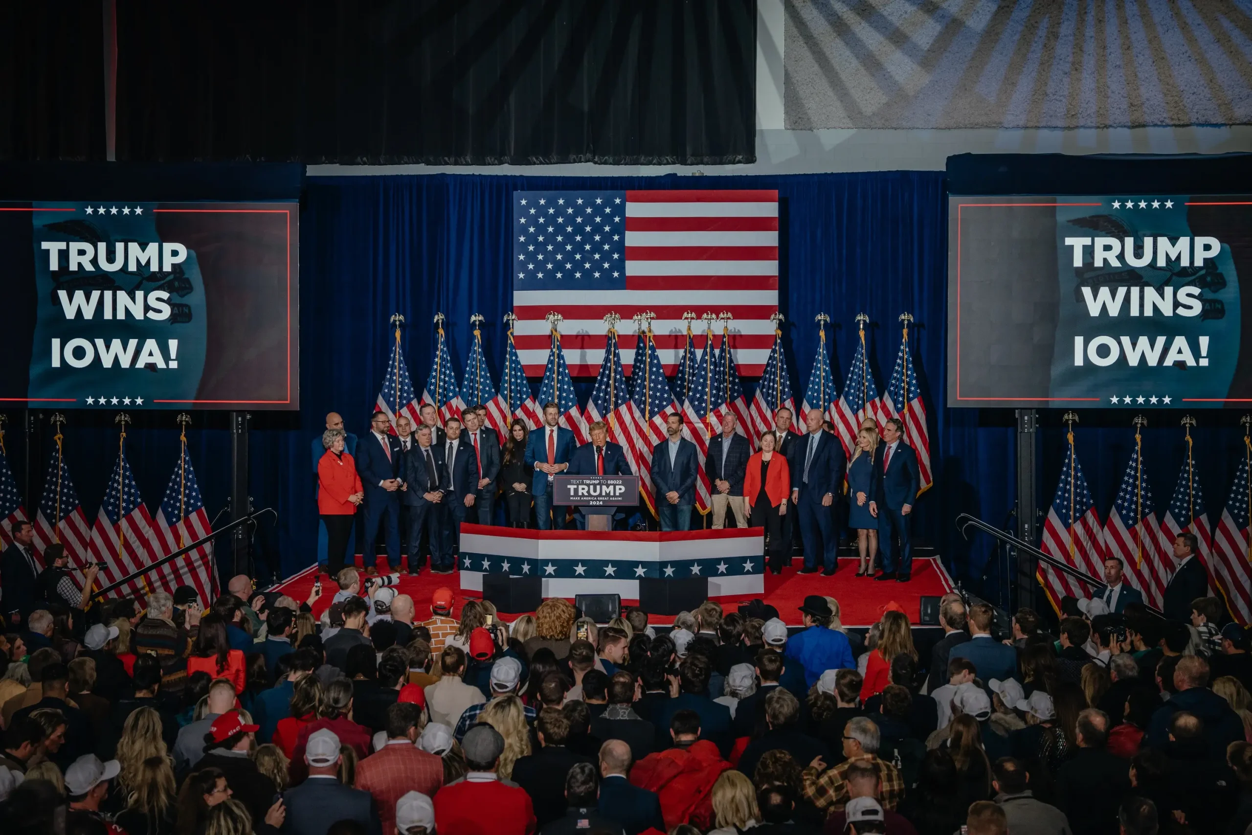 Donald Trump at a 2024 campaign rally, addressing a large crowd with American flags.