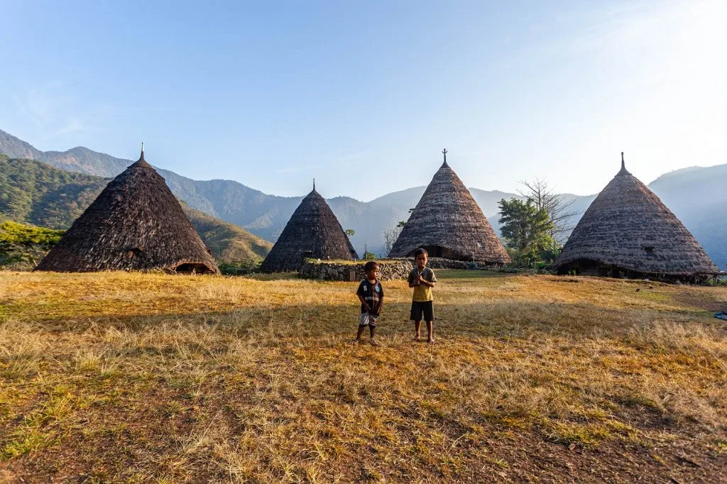 A panoramic view of Wae Rebo Village nestled amidst mist-covered mountains and lush forests.