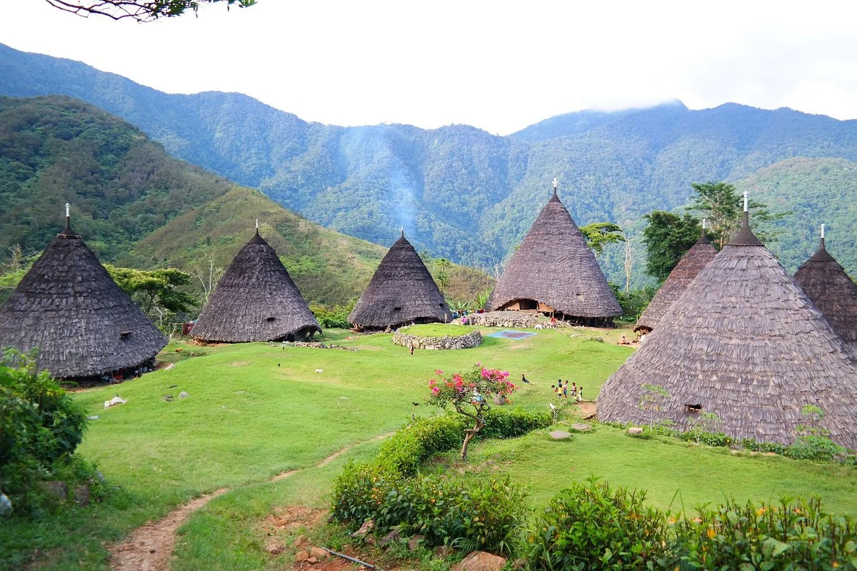 A group of visitors exploring the winding pathways of Wae Rebo Village, encountering traditional architecture and vibrant culture